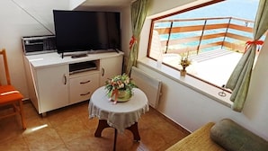 Un espace de vie compact comprenant une télévision, une petite table agrémentée d’un arrangement floral, un canapé et une fenêtre donnant sur la mer.