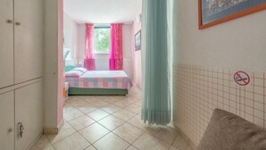A bedroom with a bed, a window with pink curtains, a door with a key, and a no-smoking sign on the wall.