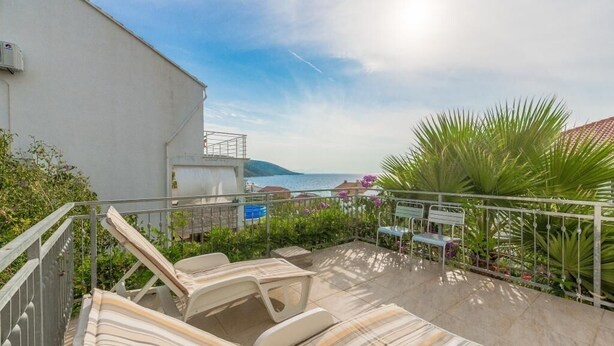 A balcony with lounge chairs and a table, overlooking a body of water and hills.