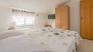 Ein Schlafzimmer mit einem Bett, einem Kleiderschrank, einem Fernseher und einem Fenster mit Vorhängen.