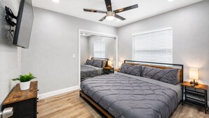 A bedroom with a bed, bedside tables, a ceiling fan, a TV mounted on the wall, and a potted plant. - Heated Pool, 5BR Sleeps 14, Game Table | 15 Min to Busch Gardens, Tampa (Tampa)