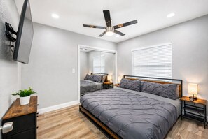 A bedroom with a bed, bedside tables, a ceiling fan, a TV mounted on the wall, and a potted plant. - Spacious, Modern and Fully Updated Gorgeous Home (Tampa)