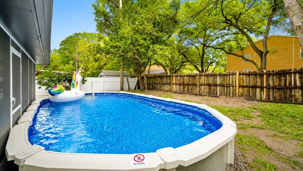 A backyard with a swimming pool, inflatable float, and a wooden fence. - Heated Pool, 5BR Sleeps 14, Game Table | 15 Min to Busch Gardens, Tampa (Tampa)