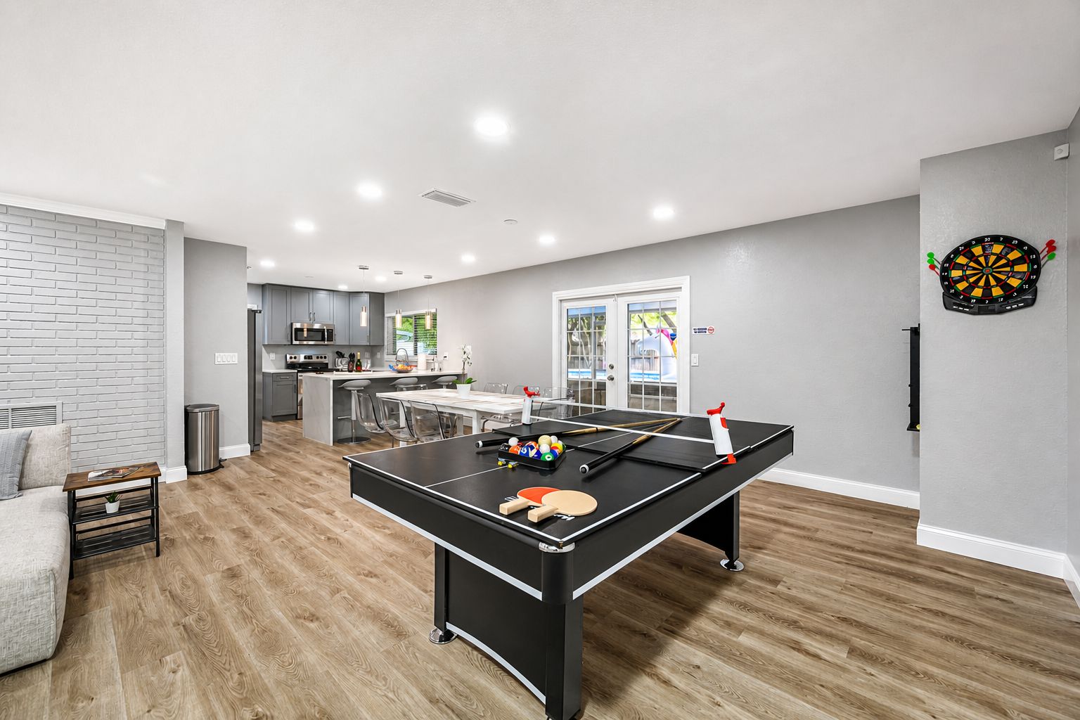 A modern living room with a foosball table, a dartboard, and a kitchen area in the background.