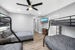 A room with bunk beds, a ceiling fan, a television, and a wooden floor. - Heated Pool, 5BR Sleeps 14, Game Table | 15 Min to Busch Gardens, Tampa (Tampa)