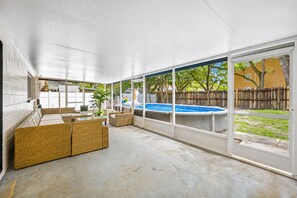 A covered patio area with a pool, wicker furniture, and a view of the backyard.