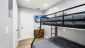 Une chambre avec un lit superposé, une porte blanche, une petite armoire en bois et un téléviseur fixé au mur.