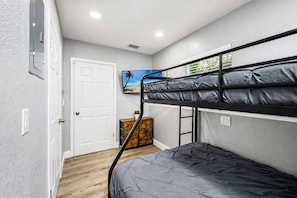 Una camera con letto a castello, una porta bianca, un piccolo armadietto in legno e una TV a parete.