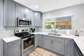 A modern kitchen with grey cabinets, a stainless steel microwave, a stove, and a window with blinds. - Heated Pool, 5BR Sleeps 14, Game Table | 15 Min to Busch Gardens, Tampa (Tampa)