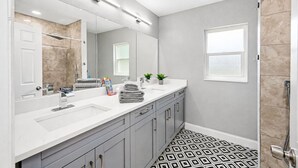 A modern bathroom with a large mirror, dual sinks, and a patterned floor. - Heated Pool, 5BR Sleeps 14, Game Table | 15 Min to Busch Gardens, Tampa (Tampa)