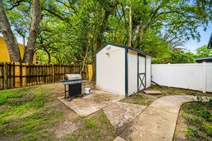 A backyard with a barbecue grill, a shed, a wooden fence, and a paved walkway. - Heated Pool, 5BR Sleeps 14, Game Table | 15 Min to Busch Gardens, Tampa (Tampa)
