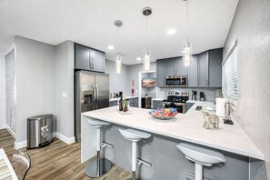 A modern kitchen with grey cabinets, stainless steel appliances, a central island with bar stools, and pendant lighting. - Heated Pool, 5BR Sleeps 14, Game Table | 15 Min to Busch Gardens, Tampa (Tampa)