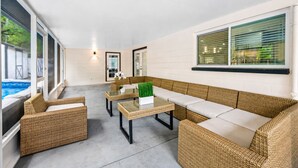 Un espace extérieur aménagé, abrité et doté de meubles en osier et d’une table en verre, offrant une vue sur une piscine.