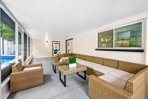 Area salotto esterna coperta con mobili in vimini e un tavolo in vetro, con vista su una piscina.