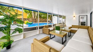 A modern outdoor lounge area with wicker furniture, a glass table, and a view of a swimming pool. - Heated Pool, 5BR Sleeps 14, Game Table | 15 Min to Busch Gardens, Tampa (Tampa)