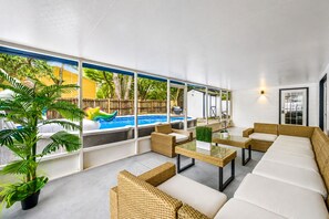 A modern outdoor lounge area with wicker furniture, a glass table, and a view of a swimming pool. - Spacious, Modern and Fully Updated Gorgeous Home (Tampa)