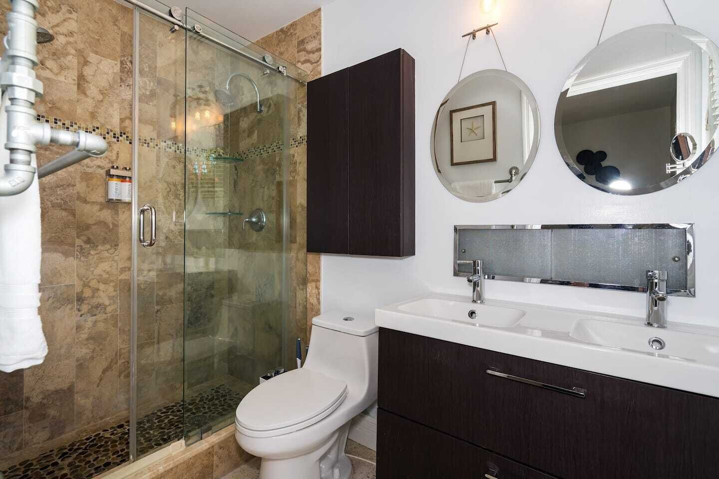 Een moderne badkamer met een douche met glazen wand, een toilet, een dubbele wastafel en een grote spiegel.