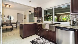 A modern kitchen with dark wood cabinets, a stainless steel dishwasher, and a large window offering a view of greenery.