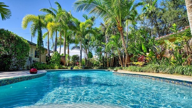 A swimming pool surrounded by lush tropical vegetation and a building with a tiled roof.