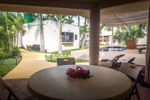 A covered outdoor area with a round table and chairs, a small pool, and a pathway leading to a building with a window and a door.