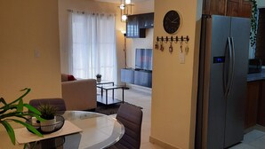 A modern kitchen with a refrigerator, a dining area with a table and chairs, and a living room with a sofa and a coffee table.