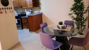 A modern kitchen with wooden cabinets, a central island with a sink, and a dining area with a glass table and purple chairs.