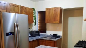 A kitchen with wooden cabinets, a stainless steel refrigerator, a microwave, and a granite countertop.