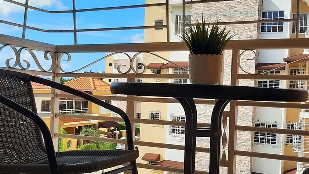 A balcony with a metal railing, a chair, a small table with a potted plant, and a view of neighboring buildings.