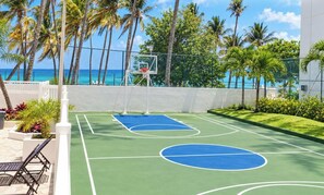 An outdoor basketball court with a view of the ocean, surrounded by palm trees and a fence. - Beachfront Walk 2 Eat Million View Location (Carolina)