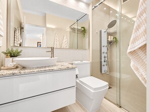 A modern bathroom with a glass-enclosed shower, a white sink, and a large mirror.