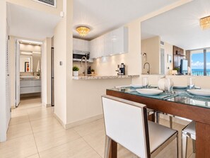 A modern kitchen with a dining area, featuring a glass-top table, white cabinetry, and a view of the sea. - Beachfront Walk 2 Eat Million View Location (Carolina)