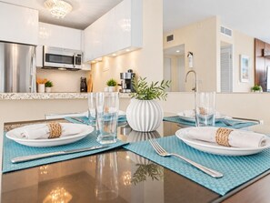 A dining table set with plates, cutlery, and glasses, with a modern kitchen in the background.