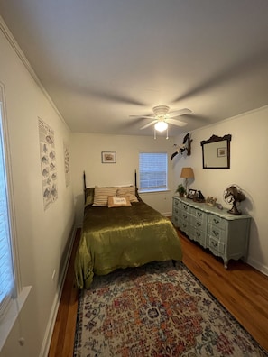 Ein Schlafzimmer mit Bett, Deckenventilator, Kommode, Fenster mit Jalousien und Wanddekorationen.