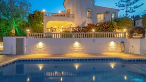 A modern villa with a swimming pool, a covered outdoor area, and a well-lit entrance.