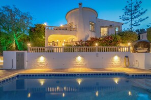A modern villa with a swimming pool, a covered outdoor area, and a well-lit entrance.