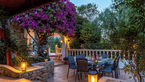An outdoor patio with a table and chairs, surrounded by stone walls and plants.