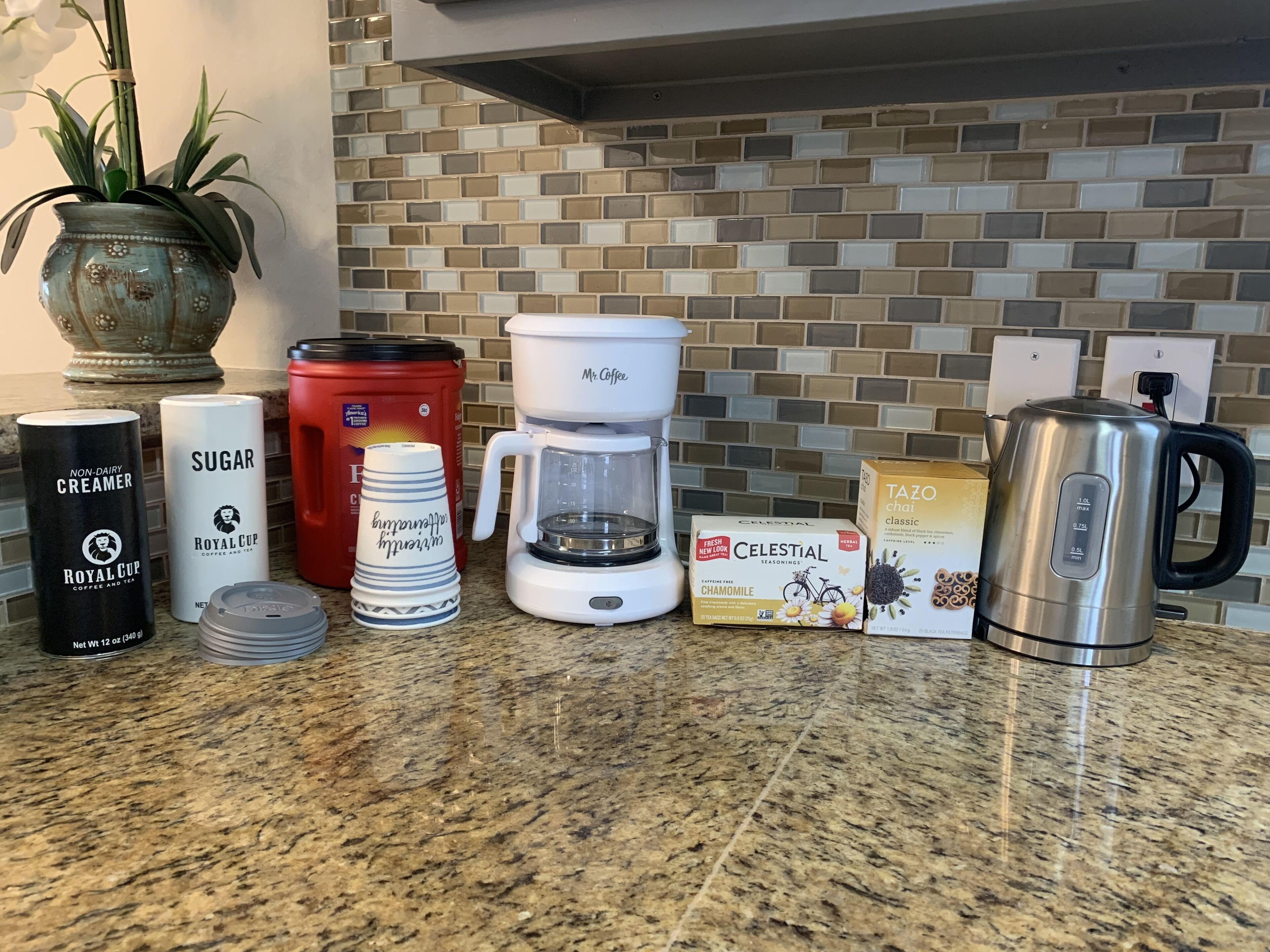 Una encimera de cocina con varios artículos, como una cafetera, un azucarero, leche condensada y cajas de té.
