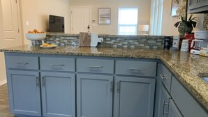 A kitchen with gray cabinets, a granite countertop, and a backsplash with small tiles. There is a bowl of fruit on the counter, a cutting board, and a potted plant. - King Bed Cozy Pet Friendly Condo with Private Terrace in a Calm Gated Community (Edinburg)