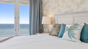 Een slaapkamer met een groot bed, een nachtkastje, een lamp en uitzicht op zee.