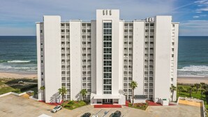 Een hoog hotel met meerdere verdiepingen, een centrale ingang en een parkeerplaats ervoor.
