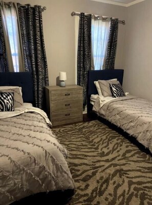 Two single beds with headboards and matching pillows, a nightstand with a lamp, and a patterned rug complete this inviting space.