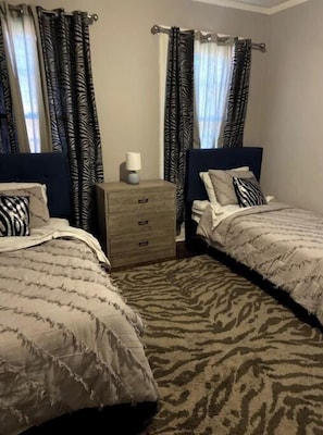 Two single beds with headboards and matching pillows, a nightstand with a lamp, and a patterned rug complete this inviting space.