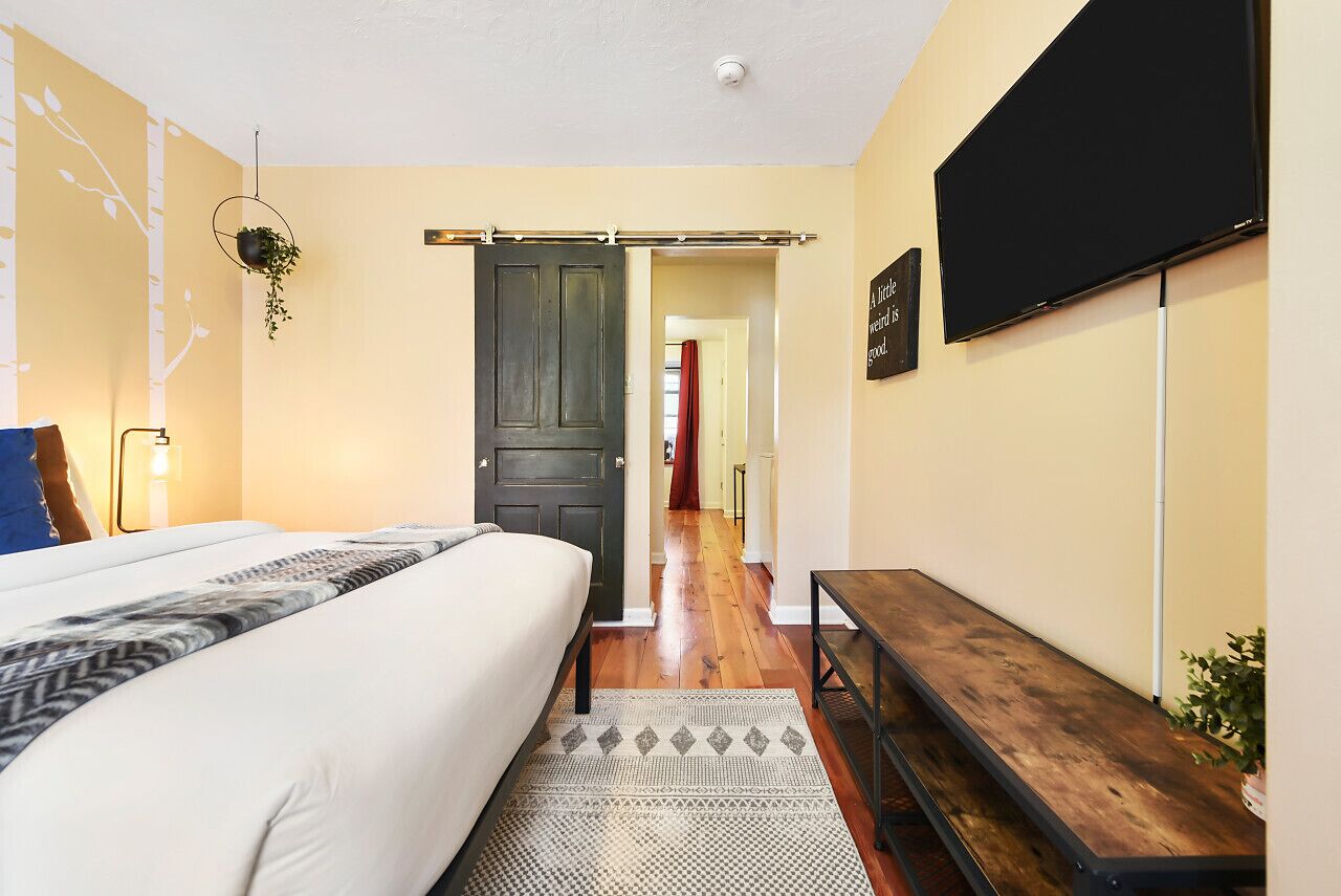 A bedroom with a bed, a bench, a TV, and a door leading to another room.