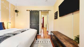 A bedroom with a bed, a bench, a TV, and a door leading to another room.