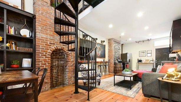 A cozy living room with a brick fireplace, a wooden dining table, and a staircase.