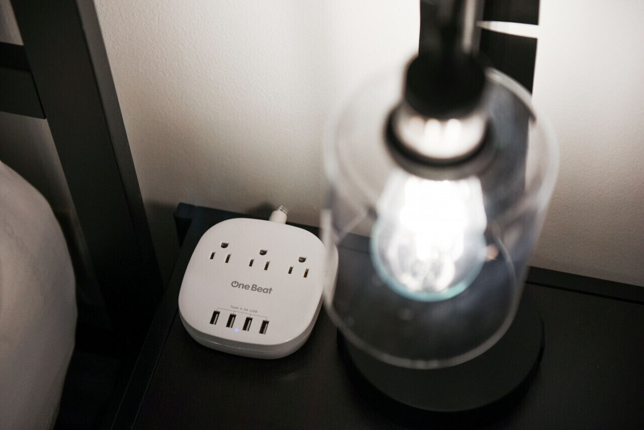 Une multiprise OneBeat et une lampe avec une ampoule visible, posées sur une table.