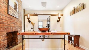 A bathroom with a wooden vanity, a large mirror, a copper basin, and a brick wall.