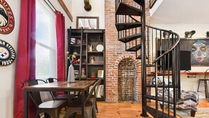 A dining area with a brick fireplace, a spiral staircase, and a bookshelf with various items.