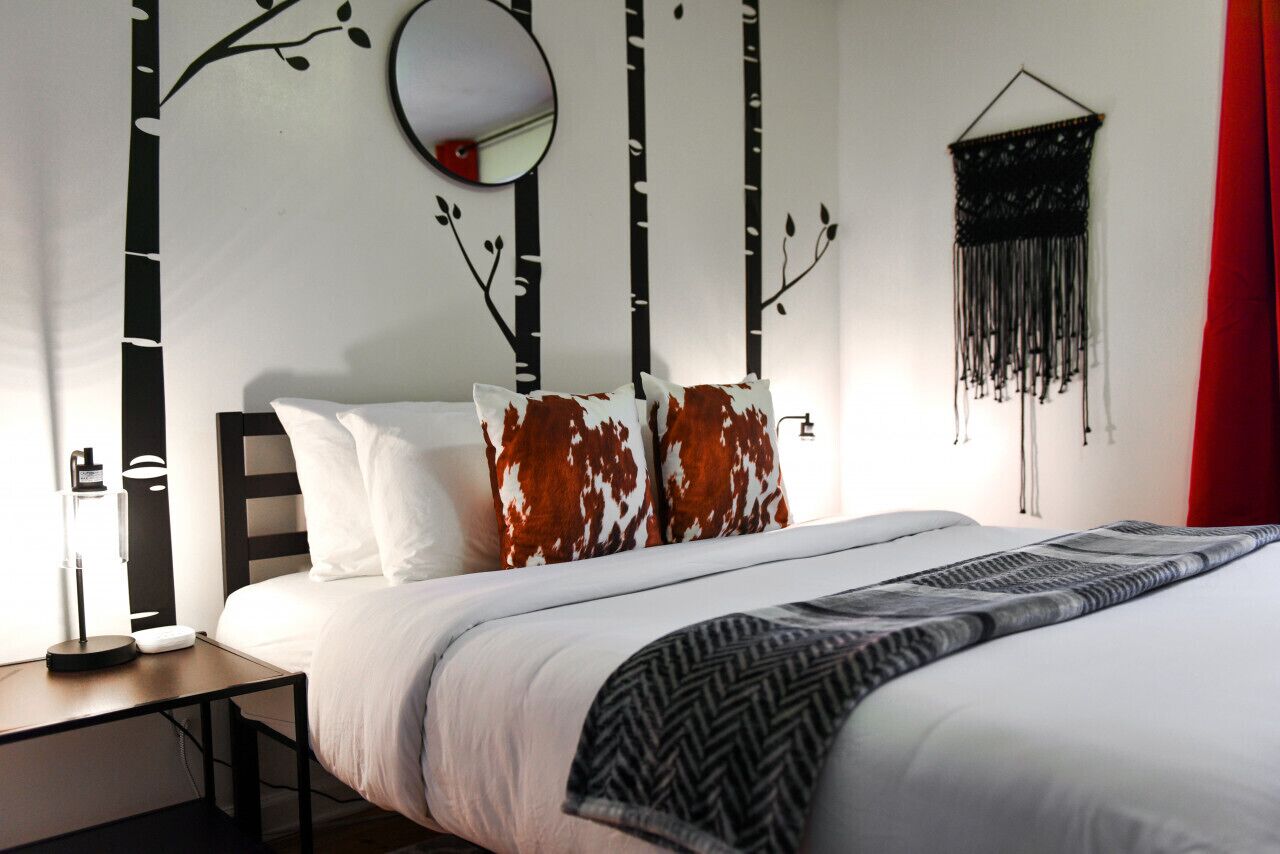 Un dormitorio con cama, mesita de noche, lámpara, espejo y decoración en la pared.
