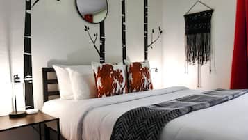 Un dormitorio con cama, mesita de noche, lámpara, espejo y decoración en la pared.